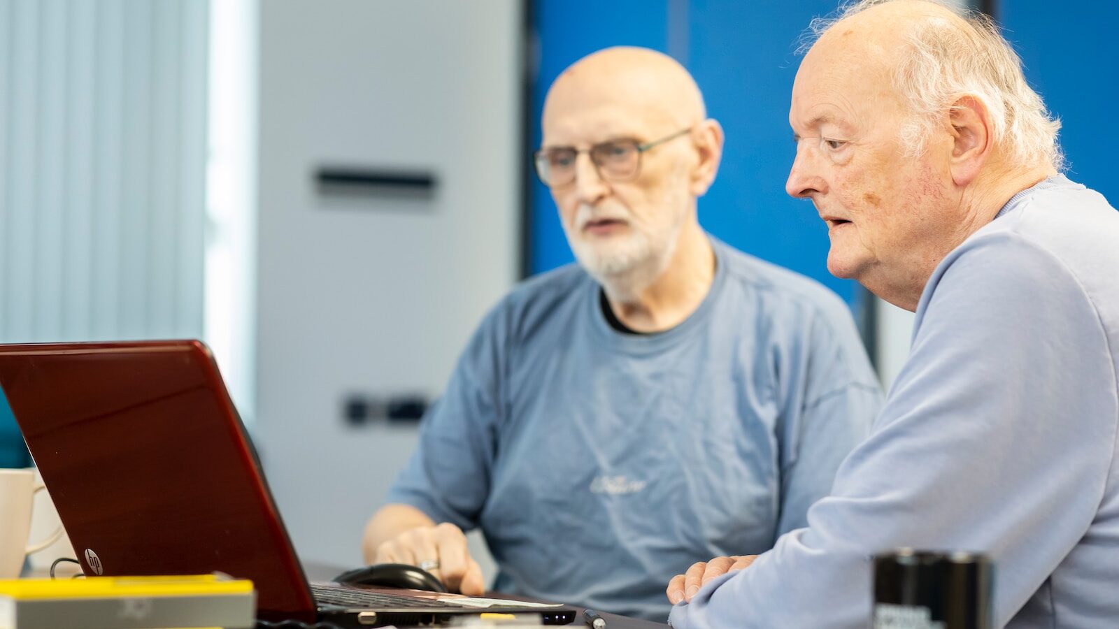 two men sitting at a table looking at a laptop